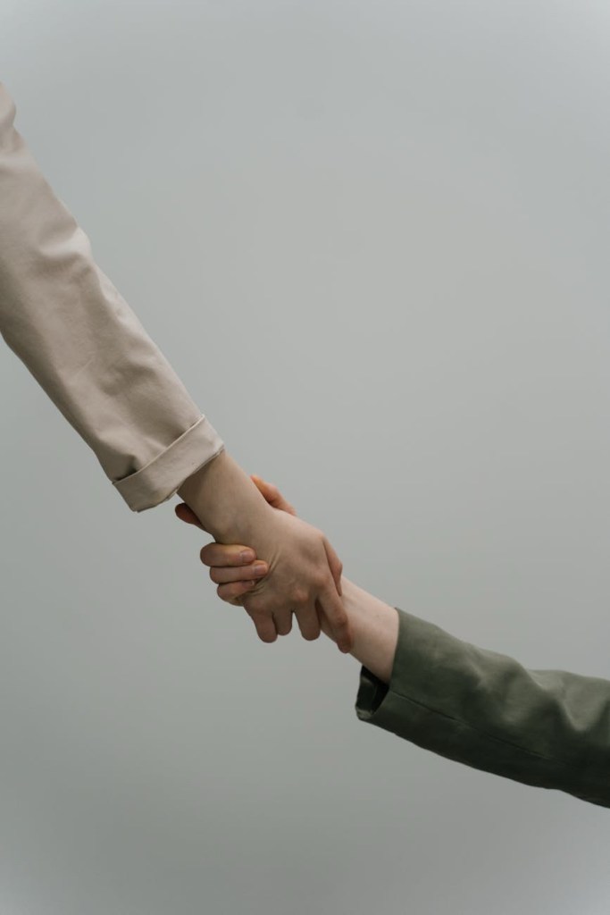 Two people are clasping hands in a supportive gesture.